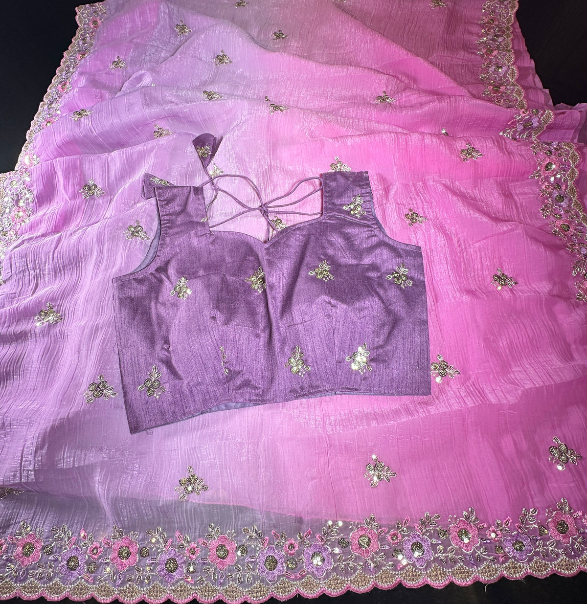 A pink and purple gradient saree with floral embroidery and a matching blouse laid flat on a dark surface.